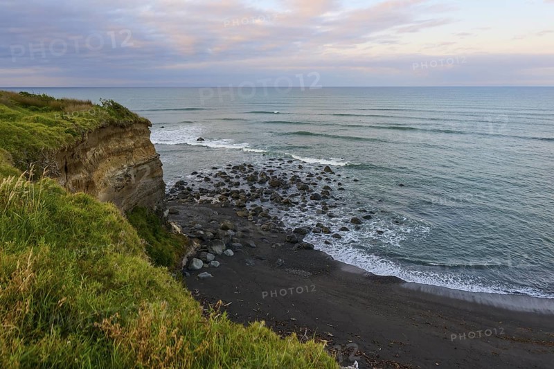 Seaside cliff with rocks and green vegetation under a cloudy sky, summer, Opunake, Taranaki, North Island, New Zealand