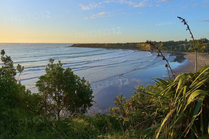 Malibu-like bay by the sea with gentle waves under a clear sky at sunset, summer, Opunake, Taranaki, North Island, New Zealand