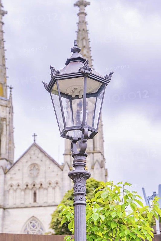 A filigree street lamp in front of an impressive church with Gothic elements under a cloudy sky, Baden Baden, Germany