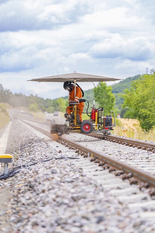 Worker working on the track with a machine under a canopy in a scenic setting, grinding work on the Hermann Hesse railway, Ostelsheim, district of Calw, Germany