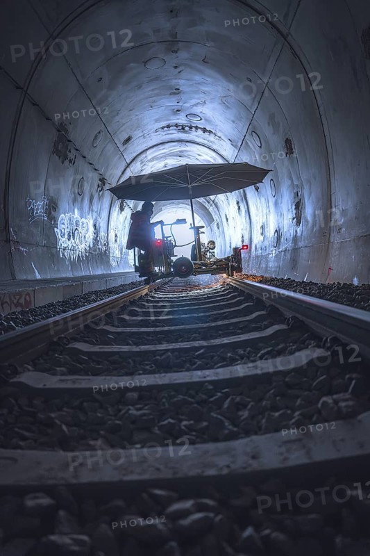 A mysterious tunnel with rails and graffiti, illuminated by a diffuse light. A figure stands under an umbrella, grinding work on the Hermann Hesse railway, Ostelsheim, district of Calw, Germany
