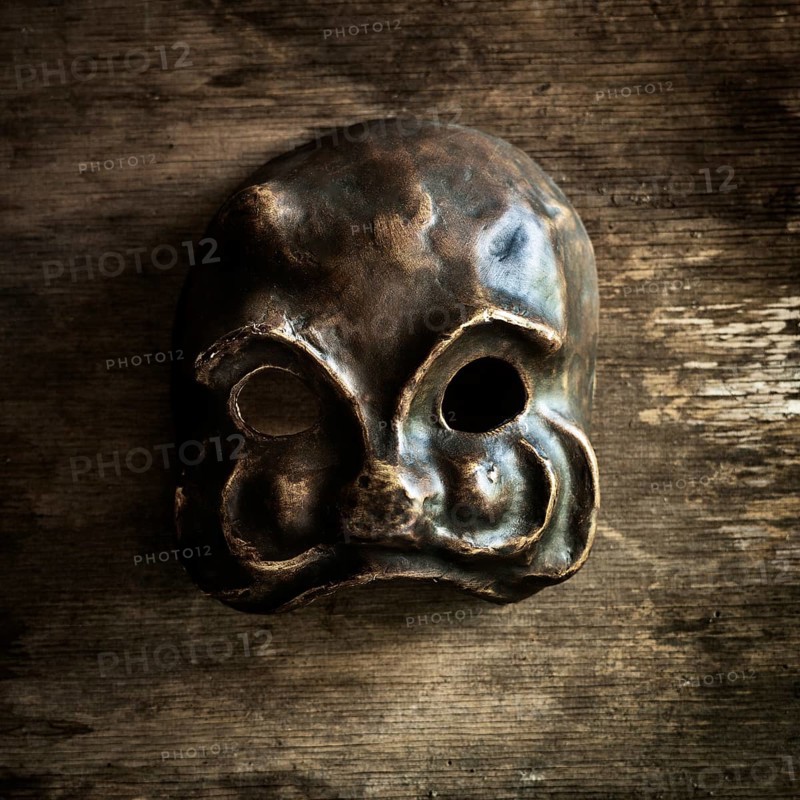 A handcrafted skull mask rests on a weathered wooden surface, highlighting its unique shape and texture. The mask features hollow eye sockets and a distinct design, emphasizing artistry