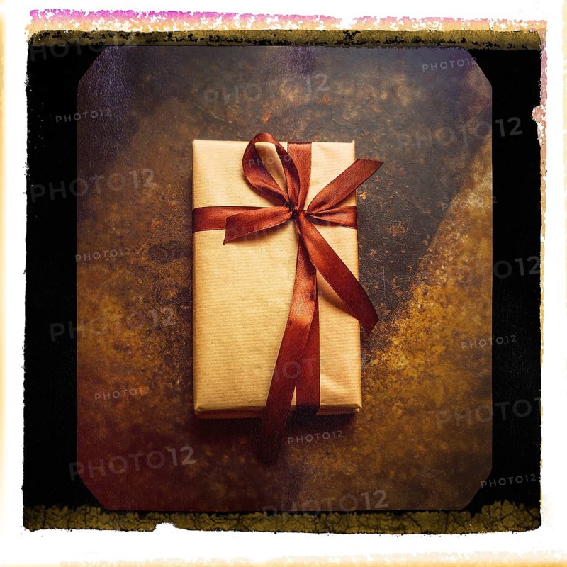 A close-up of a gift parcel elegantly wrapped in brown paper and tied with a satin ribbon, resting on a textured rustic surface in a warm, inviting environment