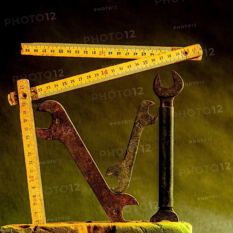 Vintage wrenches and wooden tape measures are arranged creatively against a dark, textured background, showcasing the beauty of old craftsmanship and tools used by artisans