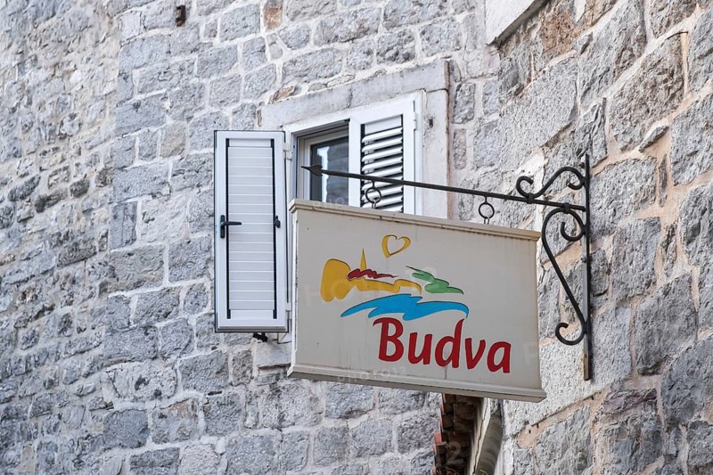Nose sign with stylised landscape and heart on a stone wall near a window with wooden shop, Budva, Montenegro