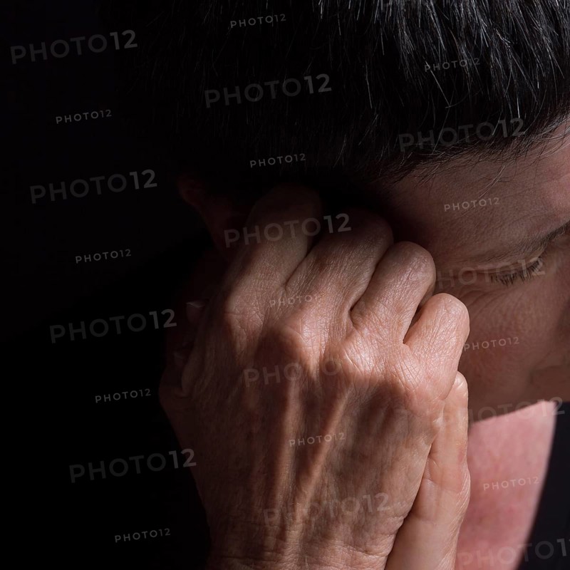 A woman with short hair rests her head on her hand, conveying deep contemplation and introspection in low lighting, creating a somber atmosphere in an intimate setting