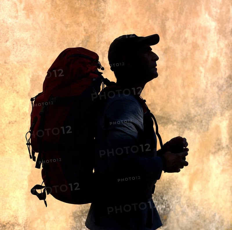 A silhouette of a walker stands against a vibrant, textured backdrop, holding supplies in hand, ready for an outdoor exploration. A large backpack indicates preparation for a journey ahead
