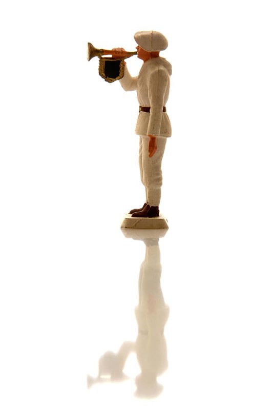 A toy soldier figurine stands in profile, wearing a white uniform and playing a trumpet. The bright background enhances the soldier's silhouette, creating an artistic display focused on the character