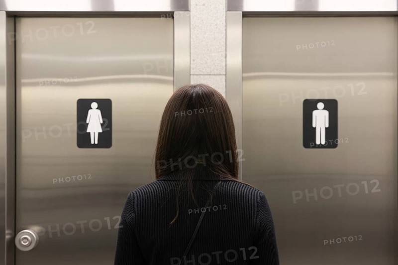 Woman in front of men's and women's bathroom doors. Concept of public restroom access and trans rights debate. Generative ai, AI generated