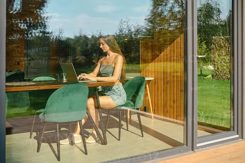 A view through the window of modern bungalow at a woman typing on laptop