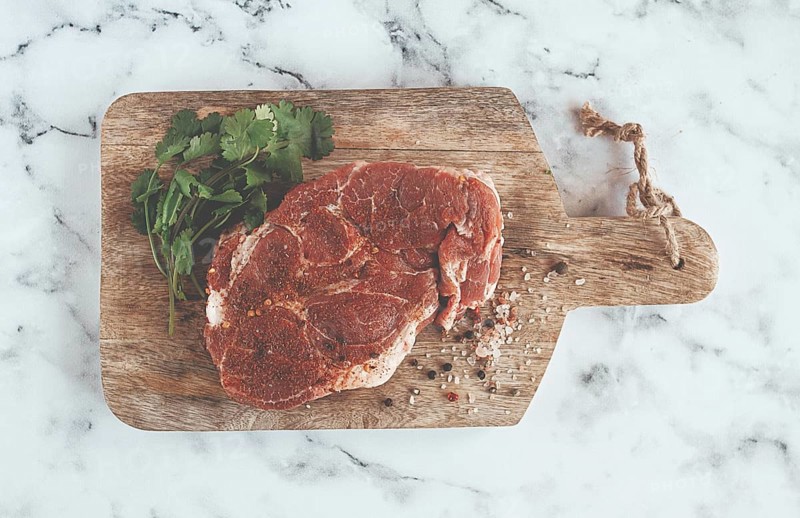 Raw pork steak, pork neck, on a chopping board, marble table, top view, with spices and coriander, no people