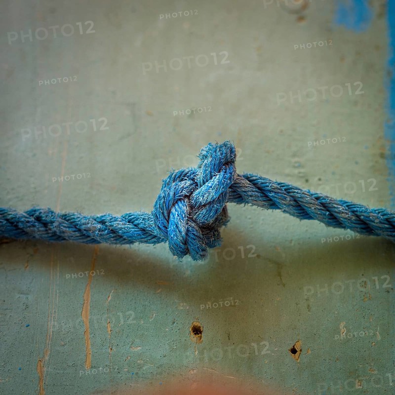 A close-up view reveals an intricately tied blue rope knot resting on a textured surface, highlighting the detailed craftsmanship involved in knot-making