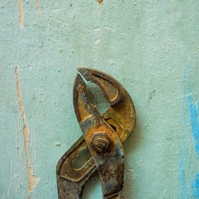 A pair of rusty pliers hangs on a worn blue wall, showcasing the wear and tear of years in a workshop setting filled with a sense of nostalgia and craftsmanship