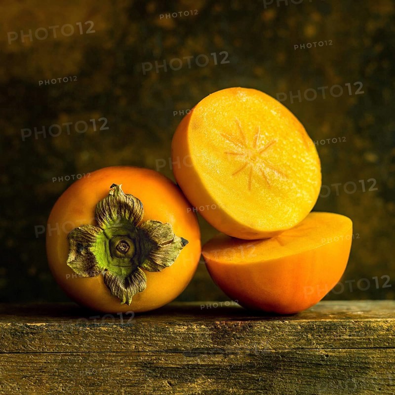Ripe persimmons are arranged thoughtfully, displaying their smooth skin and bright orange flesh. The warm lighting enhances their rich color, set against a rustic wooden background