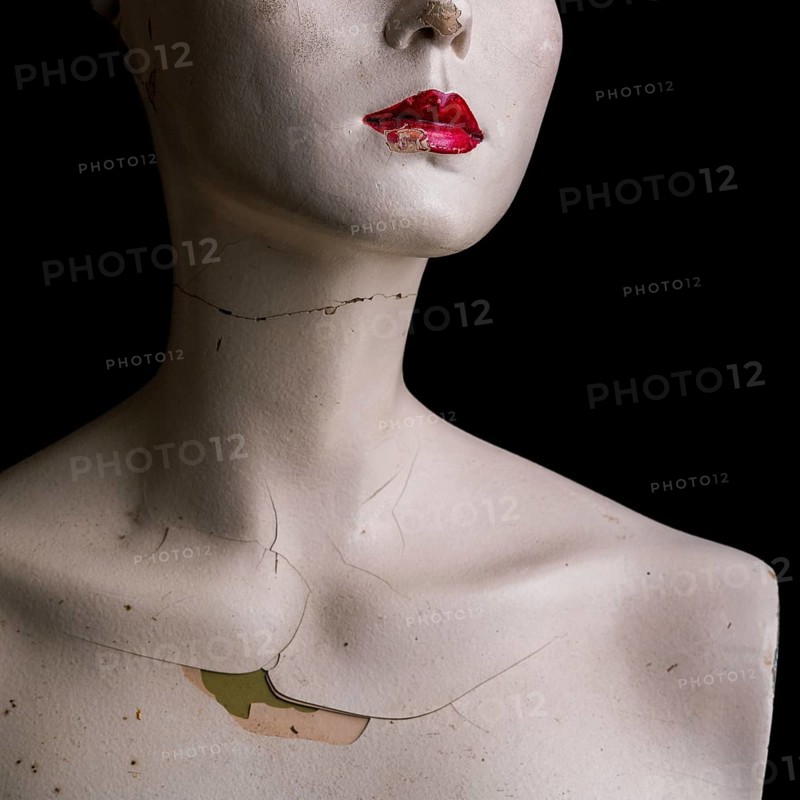 A woman dummy head showcases its vintage design with a cracked surface and a neutral expression. The dark background enhances the dummy's features and lends an artistic atmosphere