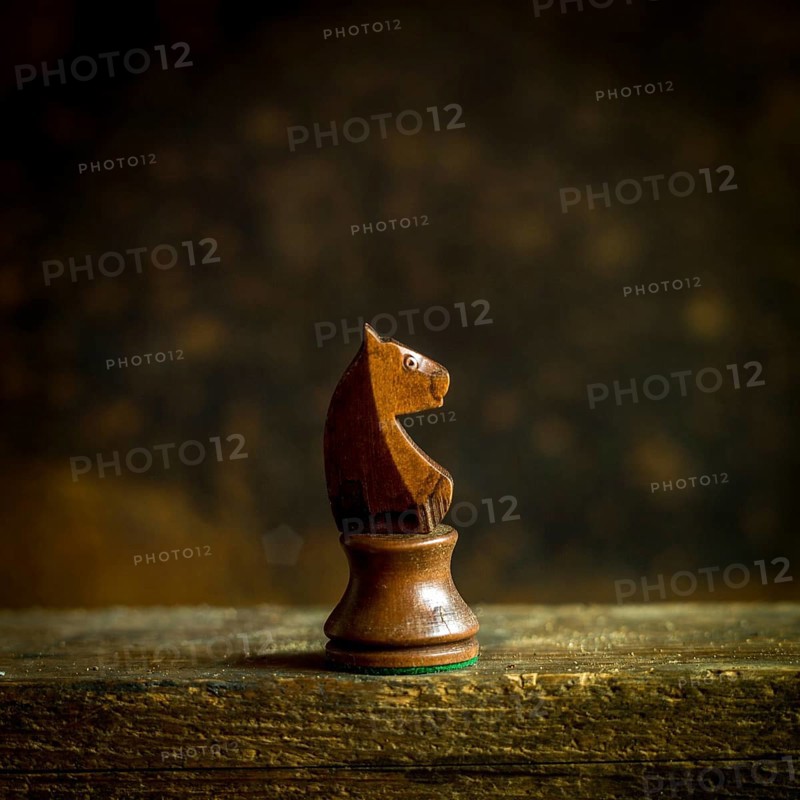 A beautifully crafted wooden chess knight piece stands prominently on a wooden surface. The backdrop is softly blurred, enhancing the warm, rustic ambiance, creating a focused view on the knight