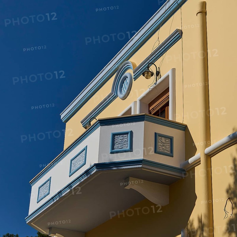 Yellow building with decorative balcony in front of a clear blue sky, Armando Bernabiti, Historicism, Rationalism, Art Deco, Rationalism, Rodolfo Petraco, Fascism, Portolago, Lakki, Leros, Dodecanese, Greek Islands, Greece