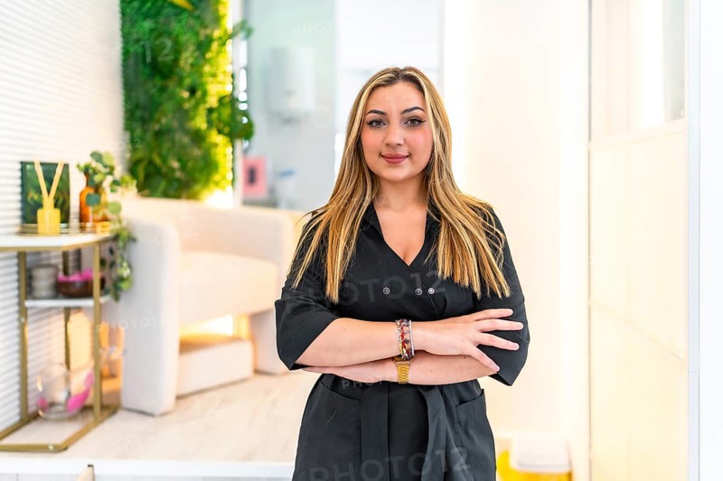 Young blond female beautician smiling with arms crossed in her beauty salon, vertical portrait