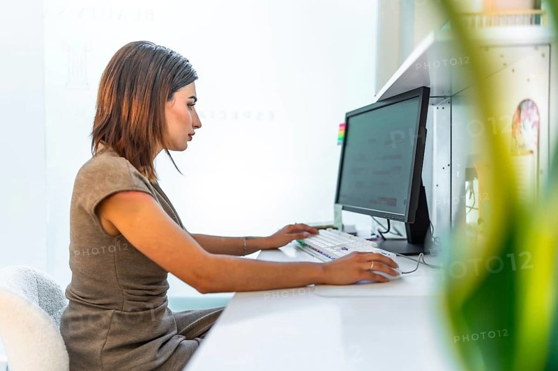 Beautician using a desktop computer, managing appointments and customer data in a bright and modern beauty salon