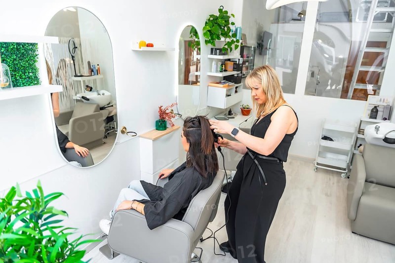 Hairdresser styling hair of female customer using curling iron in modern beauty salon, creating elegant hairstyle