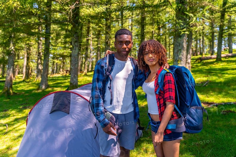 Young couple of hikers embracing and smiling next to their tent in a lush forest, enjoying a joyful camping trip together