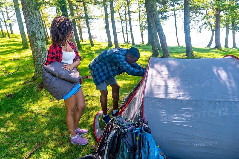 Couple setting up a tent in a lush forest, preparing their campsite for a summer adventure filled with hiking and relaxation