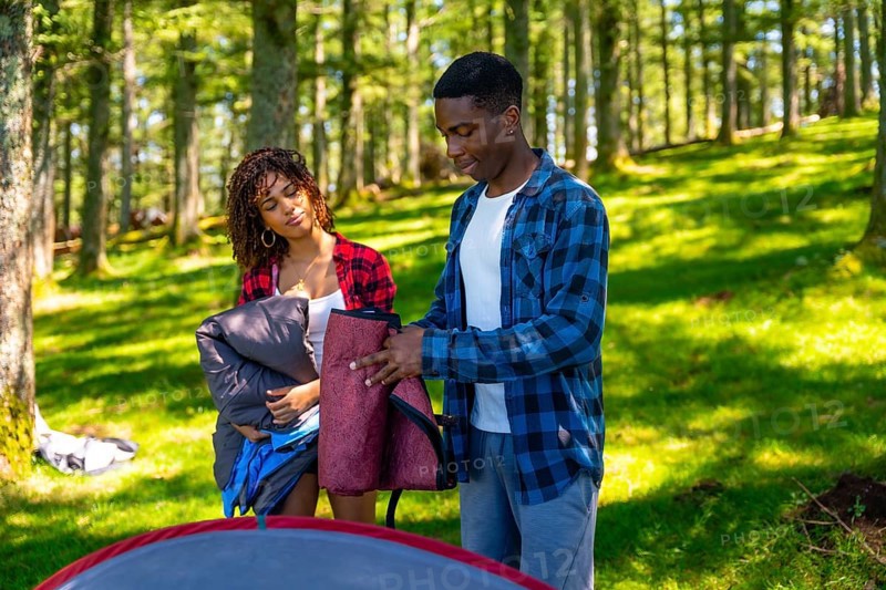 Two young campers collaborate, setting up their tent amidst a lush forest, enjoying the adventure and teamwork in the tranquil natural setting