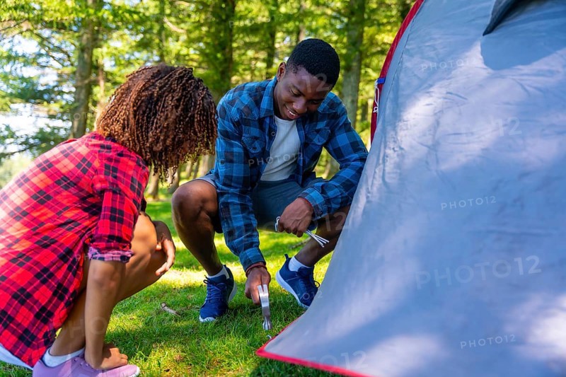 Young black couple setting up their tent in a serene forest, embracing the joy of camping and connecting with nature on a sunny day