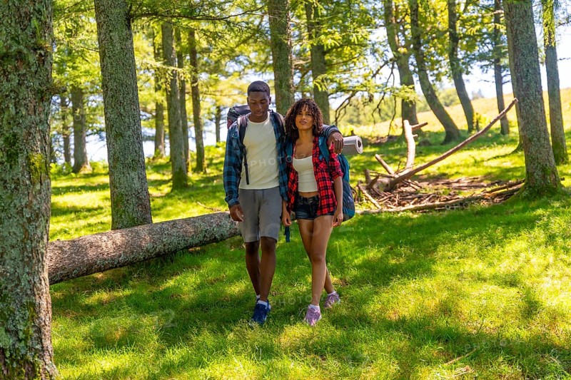 Young couple hiking through a lush forest, enjoying a summer trekking adventure filled with exploration, nature, and togetherness