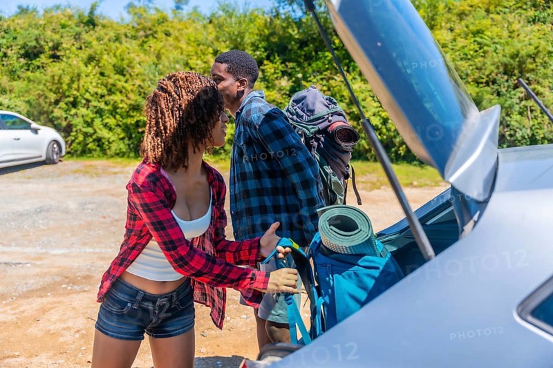 Young couple unpacking their backpacks from the trunk of the car, excitedly preparing for an adventurous hiking trip in the beautiful outdoors