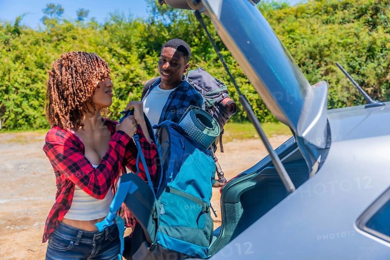 Young couple of hikers preparing backpacks next to their car before starting a trekking day in the mountains