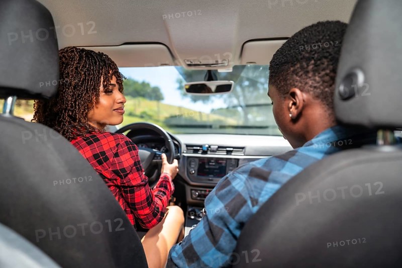 Young black couple driving a modern car on a sunny day, laughing and enjoying every moment of their exciting road trip adventure