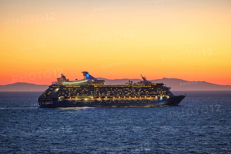 Mykonos, Cyclades, Greece - Voyager of the Seas cruise ship sails from Mykonos harbour bay towards the evening sun at dusk