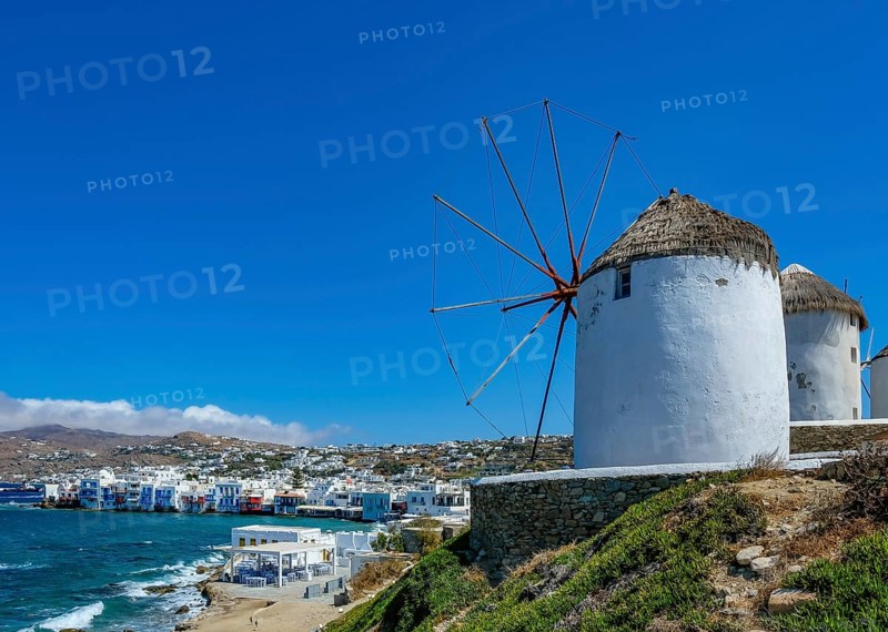 Mykonos, Cyclades, Greece - The six sixteenth-century windmills, lined up on a hill above Mykonos Town, Mykonos Chora, are the island's landmark. At the back, right by the sea, are the colorful houses of Little Venice. Mykonos is part of the Cyclades archipelago in the Aegean Sea