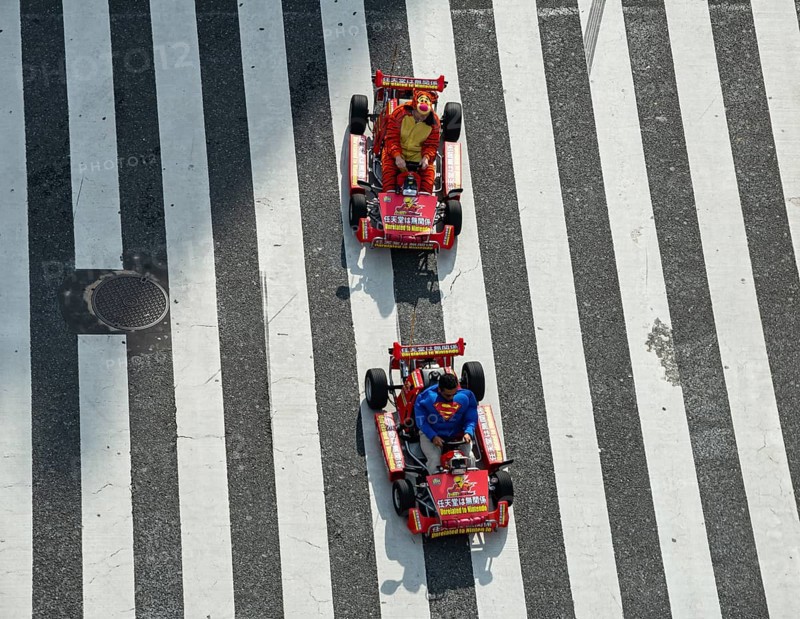 People in costumes drive small go-kart racing cars across zebra crossings, Shibuya Crossing, Shibuya, Tokyo