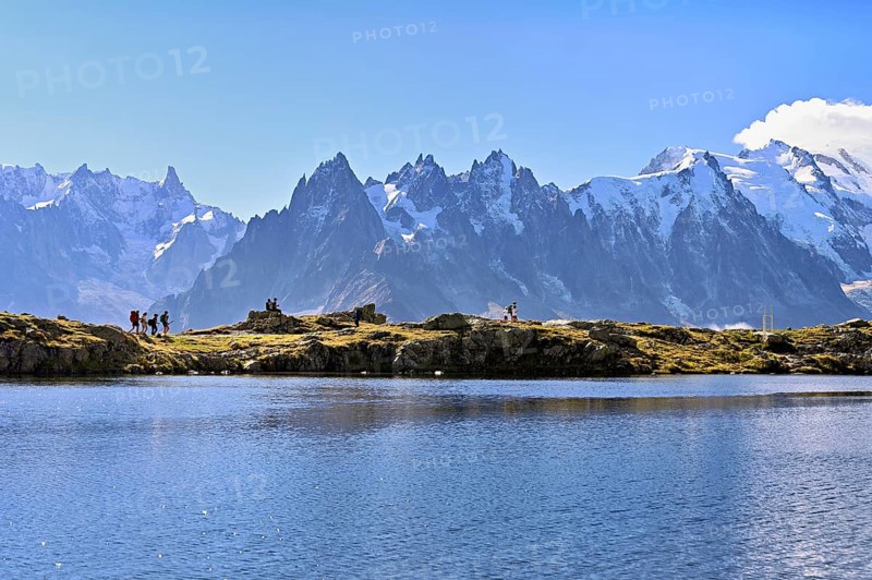 A group of hikers at Lac de Chésserys, behind the snow-covered Mont Blanc massif, Chamonix-Mont-Blanc, Haute-Savoie, France