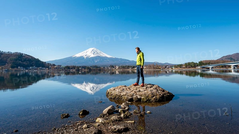 Young man standing on a rock in water, volcano Mt. Fuji is reflected in Lake Kawaguchi, Yamanashi Prefecture, Japan