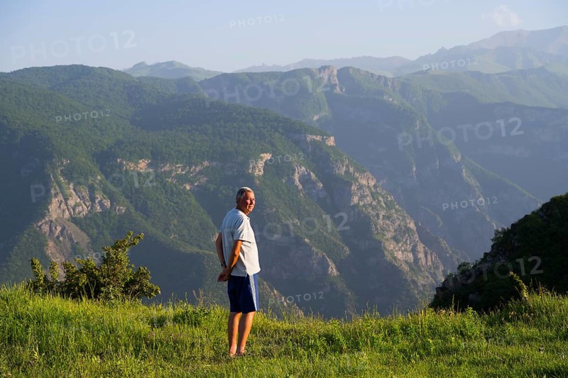 Man standing in a green field with a view of majestic mountain landscape and valley of the Vorotan River, Vorotan, Halidzor, Syunik province, Caucasus, Armenia