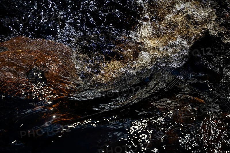 Stream flow with dark water, reflections of light and turbulence, Sweden