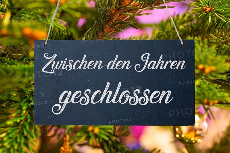 (Photo montage) Christmas holidays: sign with the inscription CLOSED BETWEEN THE YEARS in front of a Christmas tree