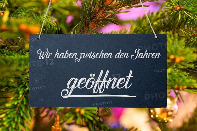 (photo montage) Christmas opening times: sign with the inscription WE ARE OPEN BETWEEN THE YEARS in front of a Christmas tree