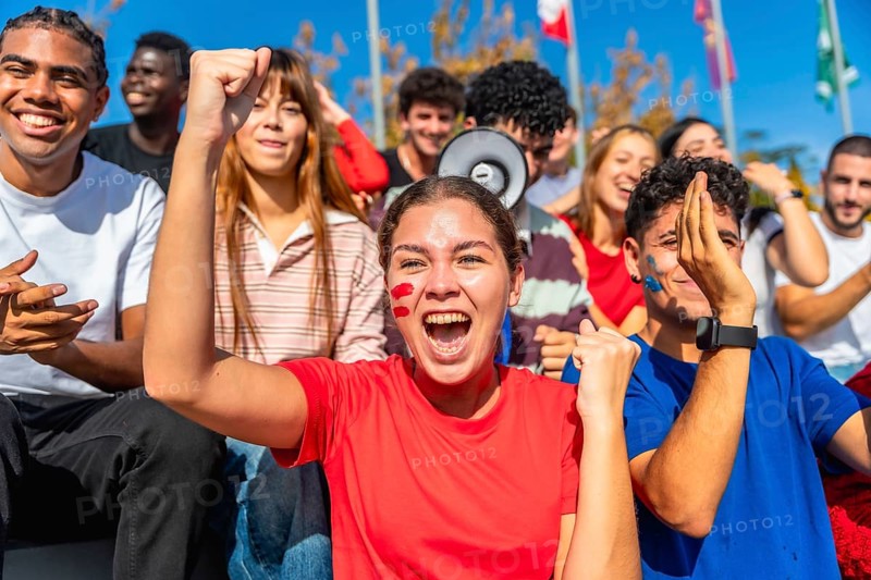 Diverse young people cheering excitedly at a stadium, wearing team colors and face paint while enthusiastically showing support for their favorite team at a sporting event