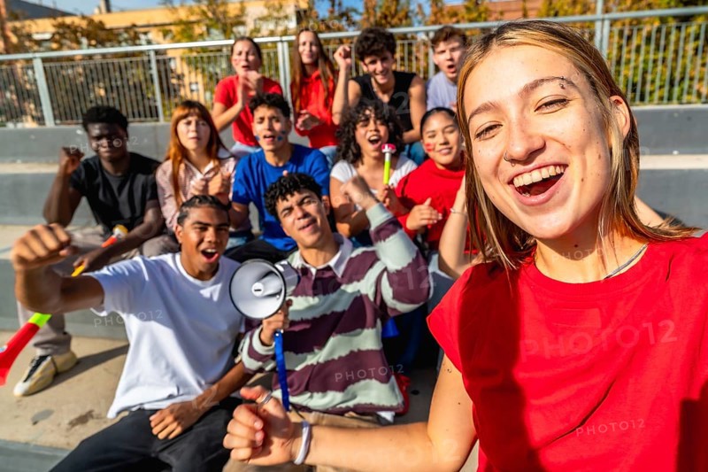 Cheering diverse group of young friends taking a stadium selfie while supporting their team, smiling and celebrating together with energy, unity and sporty excitement