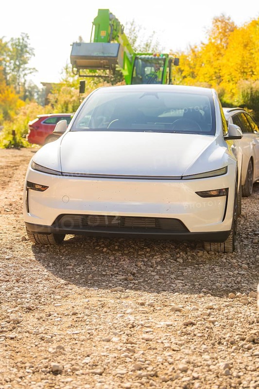 White electric car on a gravel path in autumn, surrounded by colorful foliage and trees, Telsa Model Y Juniper electric car, Gechingen, Germany
