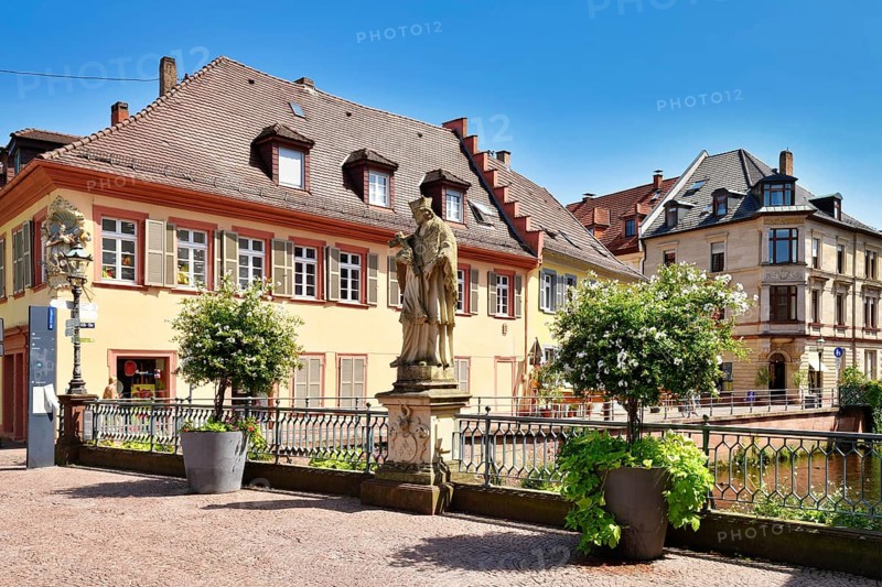 Ettlingen, Germany - August 13th 2025: Statue of Saint John of Nepomuk on Rathausbrücke bridge over River Alb with buildings in old town