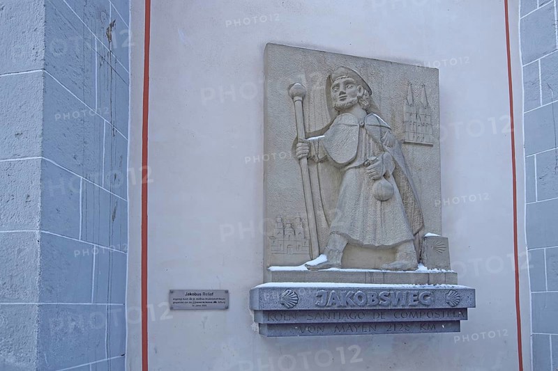 Memorial with pilgrim sculpture and stick on the Camino de Santiago de Compostela via Mayen to Santiago de Compostela, pilgrim trail, hiker, trekking, figure, stone, symbol, scallop, inscription, St. Clemens, Mayen, Vulkaneifel, Eifel, Rhineland-Palatinate, Germany