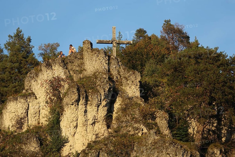 Rocky landscape with summit cross and seated hikers while resting, relaxing, rock formation, rock cliff, landscape, summit, cross, mountain, Pottenstein, Franconian Switzerland, Franconian Jura, Upper Franconia, Bavaria, Germany