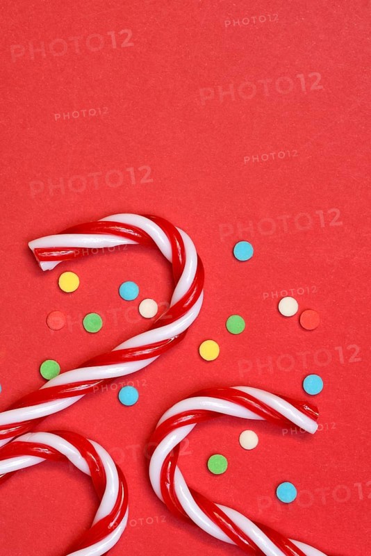 Candy canes and sugar confetti against red background, Christmas