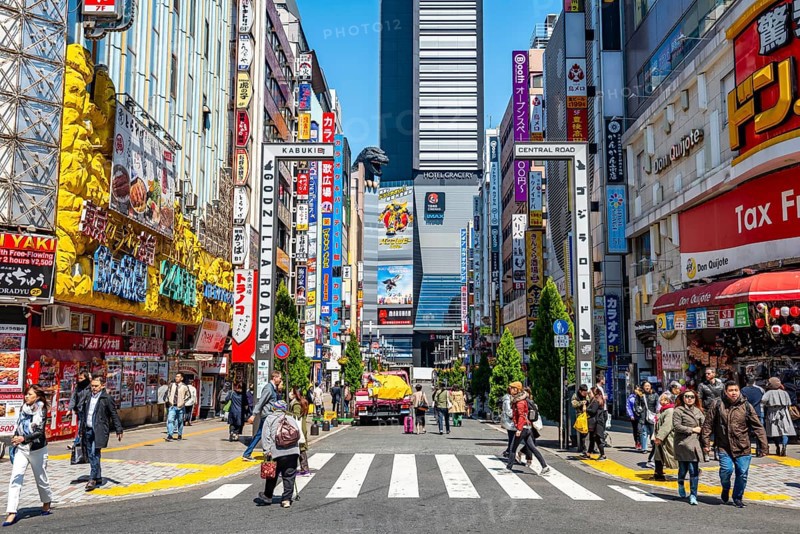 Bustling street scene in Japan with modern buildings and colorful billboards, figure of Godzilla head on a high-rise building, Shinjuku City, Tokyo, Japan
