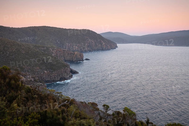The Monument. Long exposure at sunrise shows glowing dawn over the dramatic cliffs of Cape Hauy. Gentle waves hit the steep cliffs. Cape Hauy, Tasman Peninsula, Tasmania, Australia